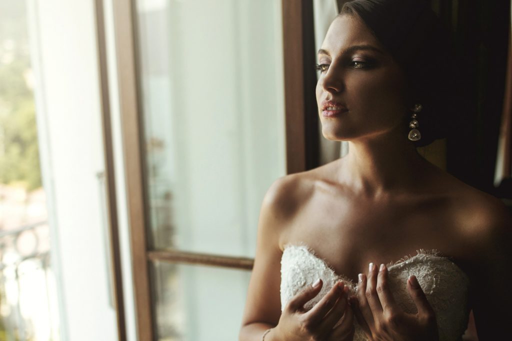 Gorgeous exotic french bride in white dress posing near window closeup